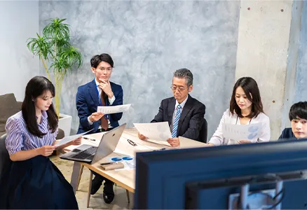 5人の社員が資料を見ながら会議をしている様子の写真