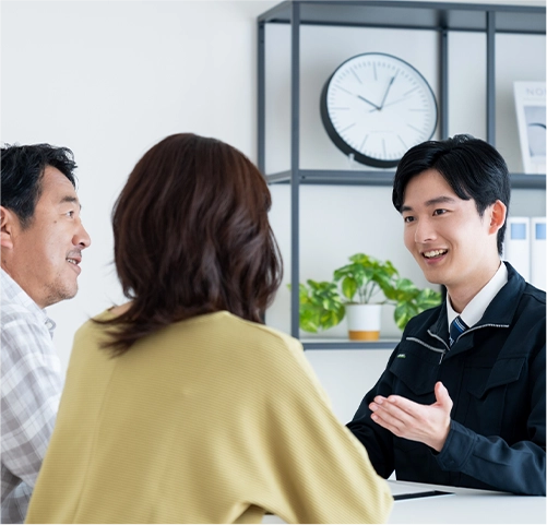作業着を着た男性スタッフが、笑顔で夫婦と会話している打ち合わせ風景の写真